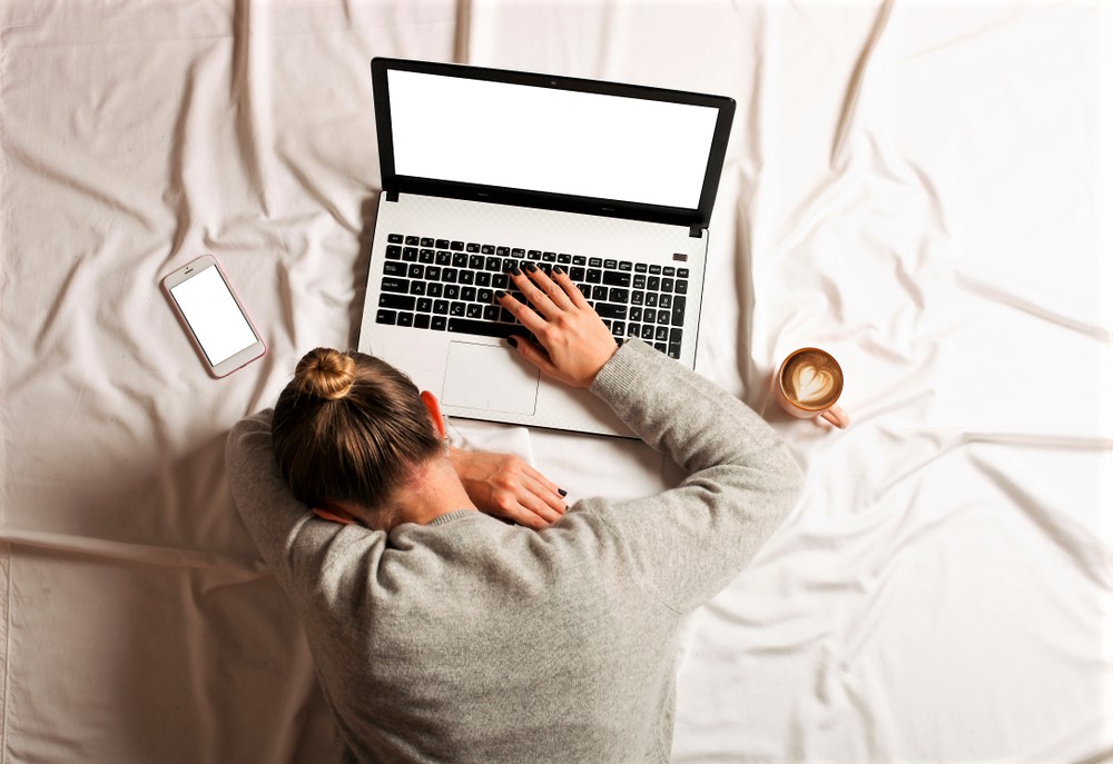 Žena drieme na posteli s kávou a počítačom