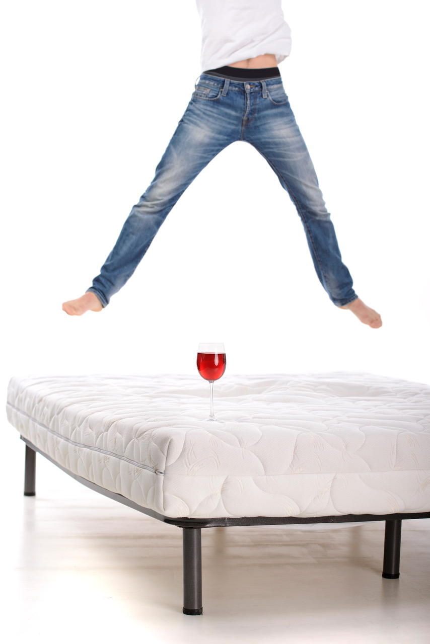 Muž skáče po matraci a pohár vína je položený na matraci.